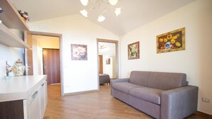 Een ruime woonkamer met een grijze bank, houten vloeren en een keukenblad.