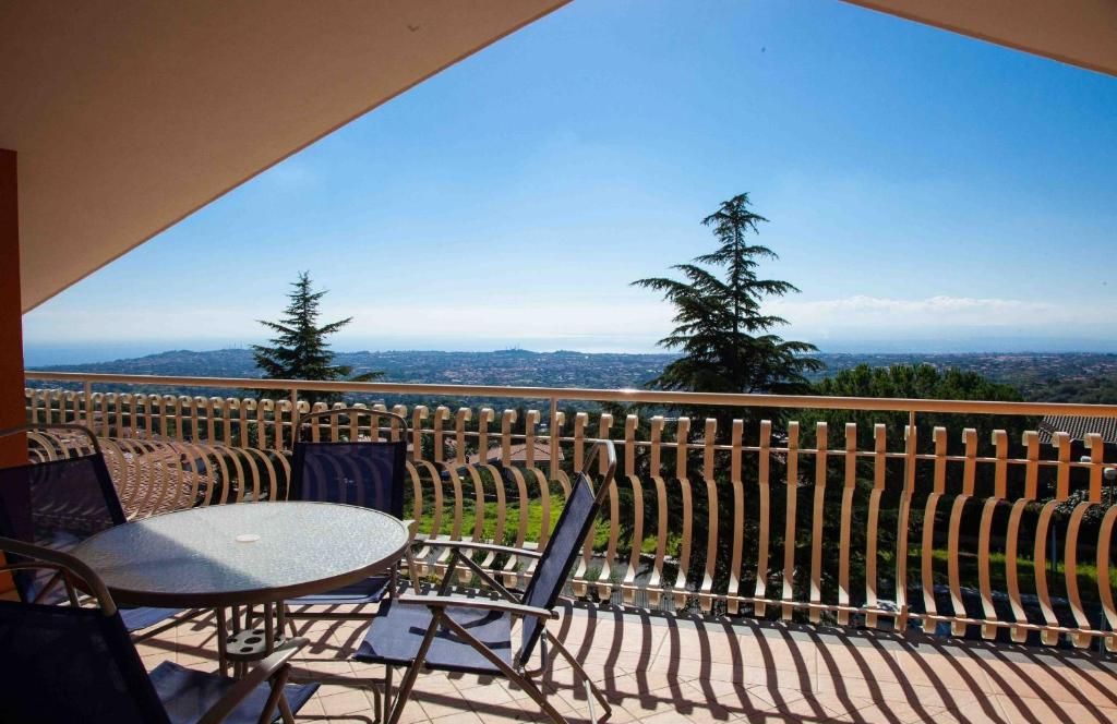 A balcony with a round table and chairs, a view of trees and distant landscape.