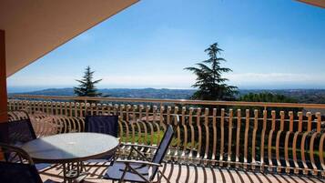 A balcony with a round table and chairs, a view of trees and distant landscape.