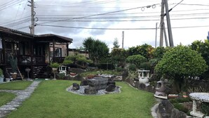 A well-maintained garden with a stone pathway, a small pond, and various potted plants. - Minshuku Teruya (Nago)