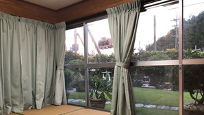 A room with tatami mats, sliding glass doors, and a view of a garden with rocks and plants. - Minshuku Teruya (Nago)