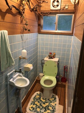 Un bagno con piastrelle blu, pavimento in legno, un water verde, un lavandino e una finestra sopra il water.