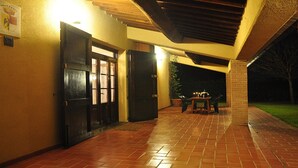Uma área externa coberta com piso de tijolos, uma mesa com cadeiras e um vaso de planta.