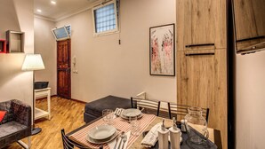 A compact room with a dining table set for two, a sofa, a lamp, and a wooden cabinet.