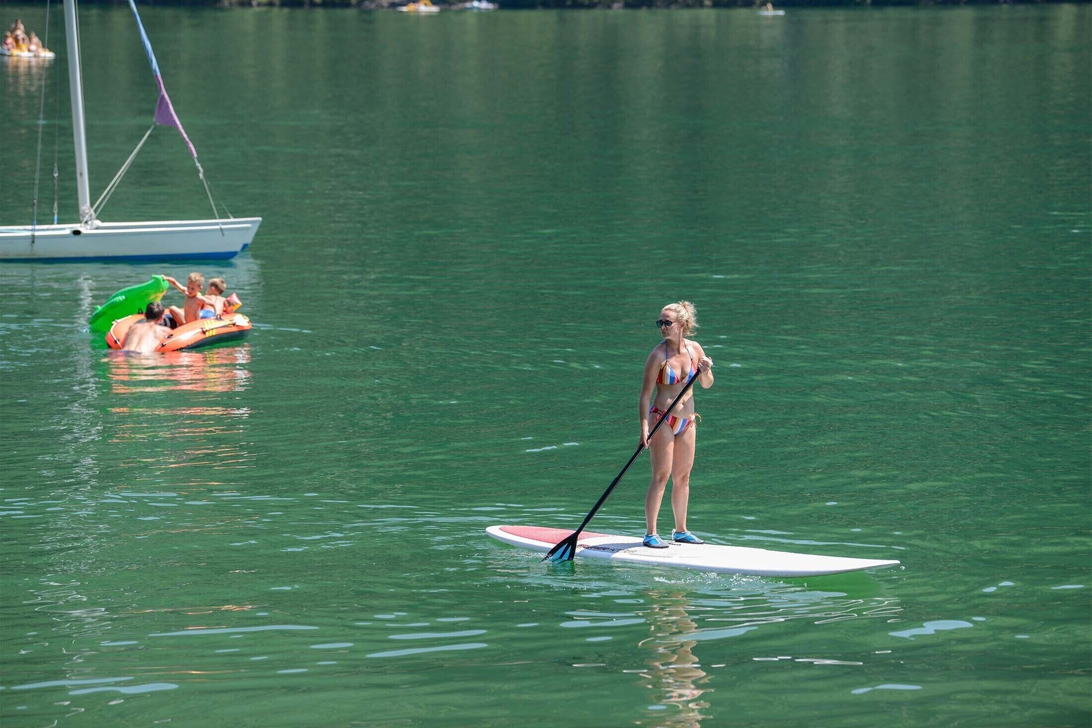 A person standing on a paddleboard in a body of water, with a sailboat in the background.