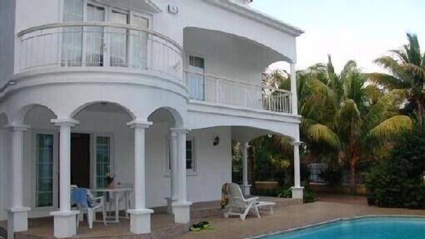 A two-story white building with a pool, outdoor seating, and palm trees.
