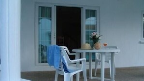A white room with a single white chair and a small table with a vase and a glass.