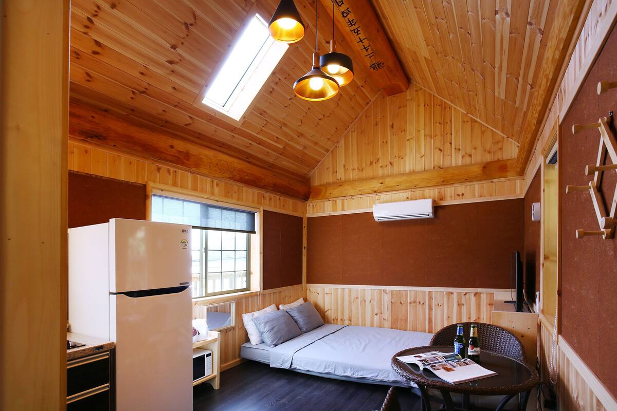 Eine kleine Holzhütte mit einem Bett, einem kleinen Schreibtisch und einem Kühlschrank.