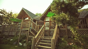 A wooden cabin with a staircase leading to a deck, surrounded by trees. - Tongyeong Daore Pension (Tongyeong)