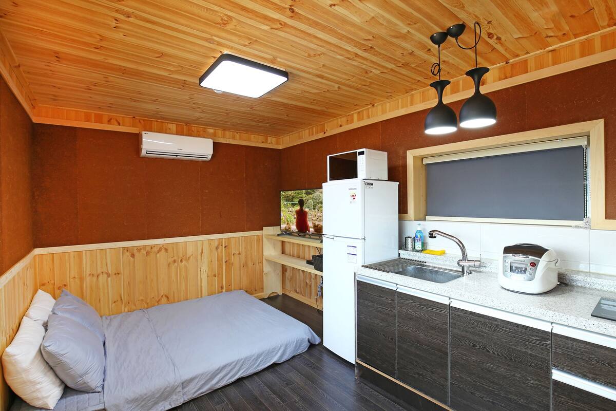Ein kleines Zimmer mit Bett, einer Küchenzeile und einem Fenster.