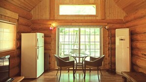 A cabin-style room with a wooden interior, a dining table with chairs, a refrigerator, and a window with bars. - Tongyeong Daore Pension (Tongyeong)