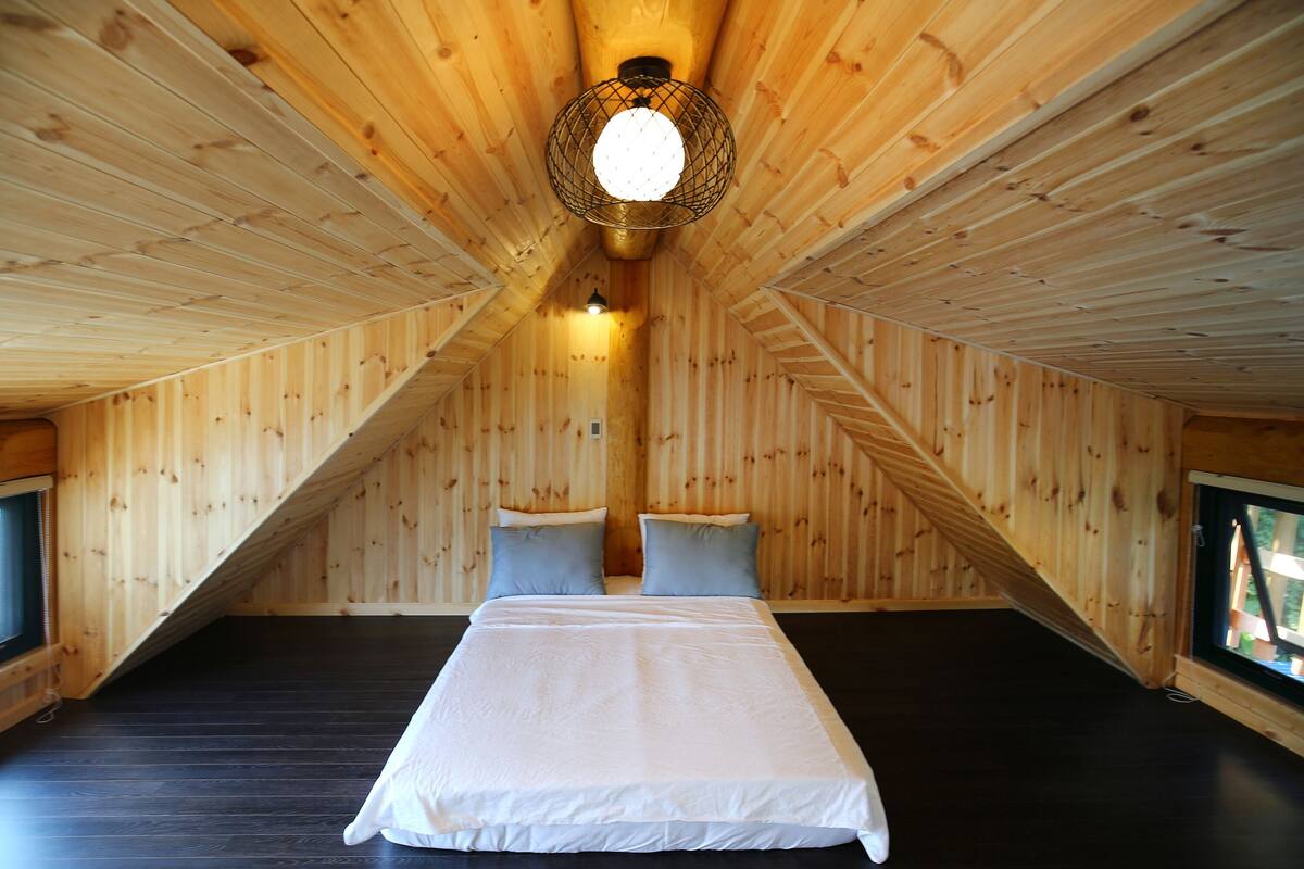 Ein Holzinnenraum mit einem Bett, Kissen und einer Hängelampe.