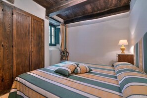 A bedroom with a bed, wooden wardrobe, window with curtains, and a bedside lamp. - Sarna Castle, Portico (Sarna, Chiusi della Verna)