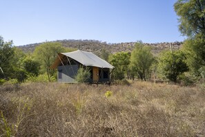 A small, modern tent-like structure in a natural setting with a clear sky and a hilly background.