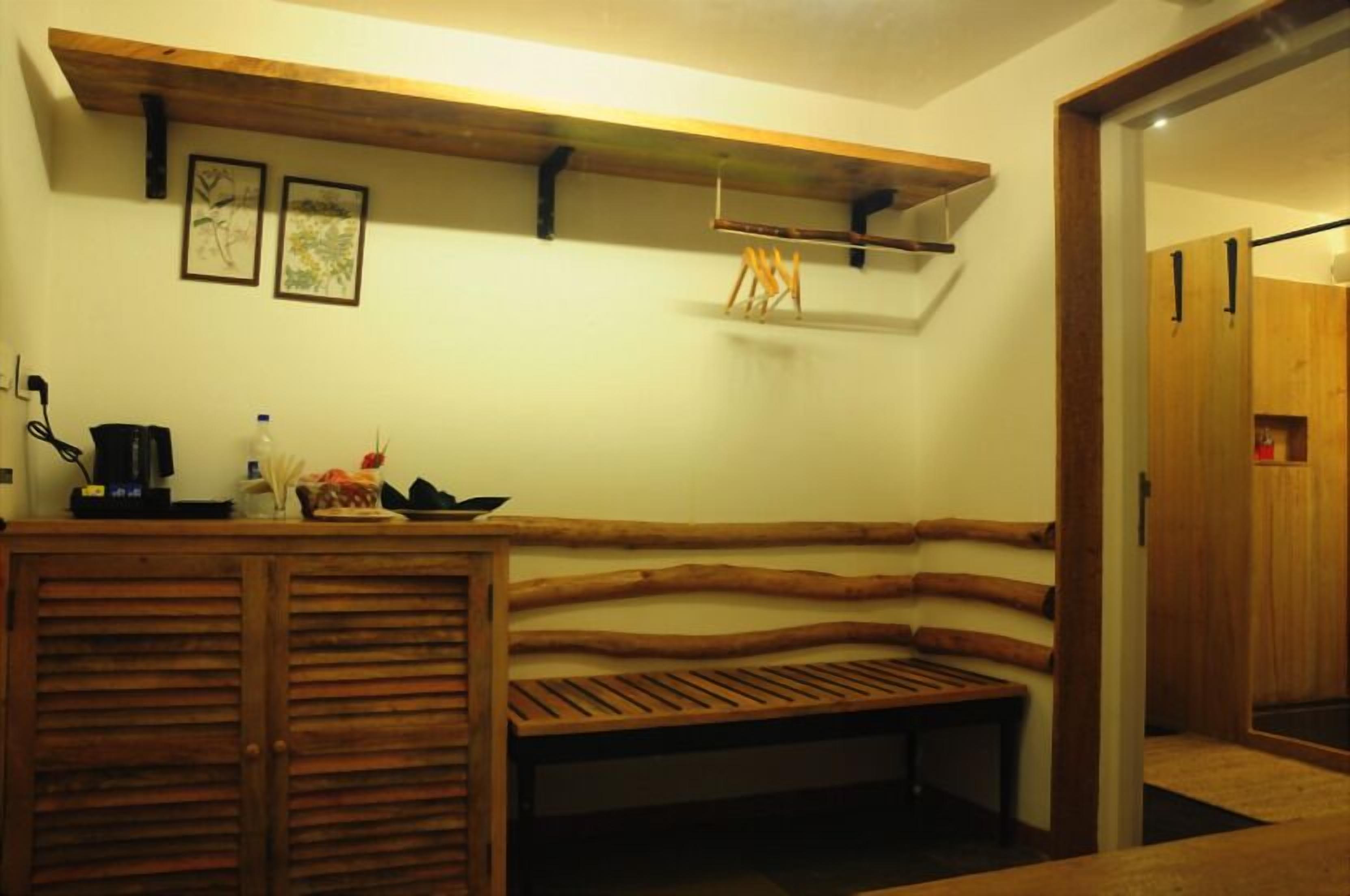 A cozy room with a wooden bench, a small table with a kettle, and a shelf with pictures.