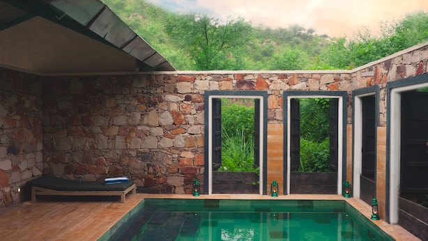 Habitación de paredes de piedra con piscina, zona de descanso y amplios ventanales con vistas al verdor.