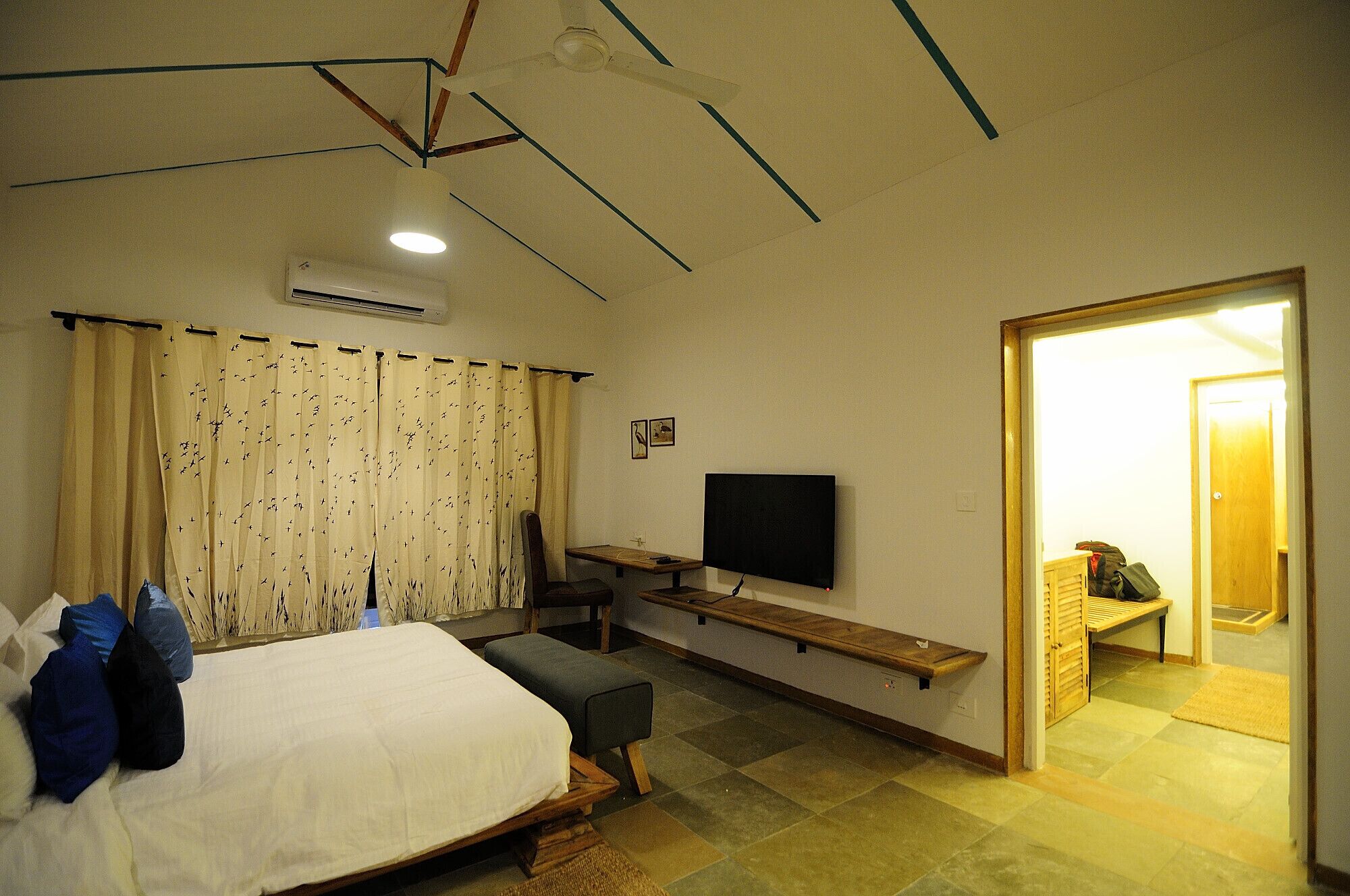 Een slaapkamer met een bed, een bureau, een stoel, een televisie en een deur naar een andere kamer.