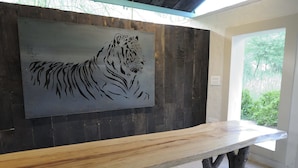 Zona de recepción con un banco de madera, una pared oscura con un mural de tigre y vistas al exterior con vegetación.