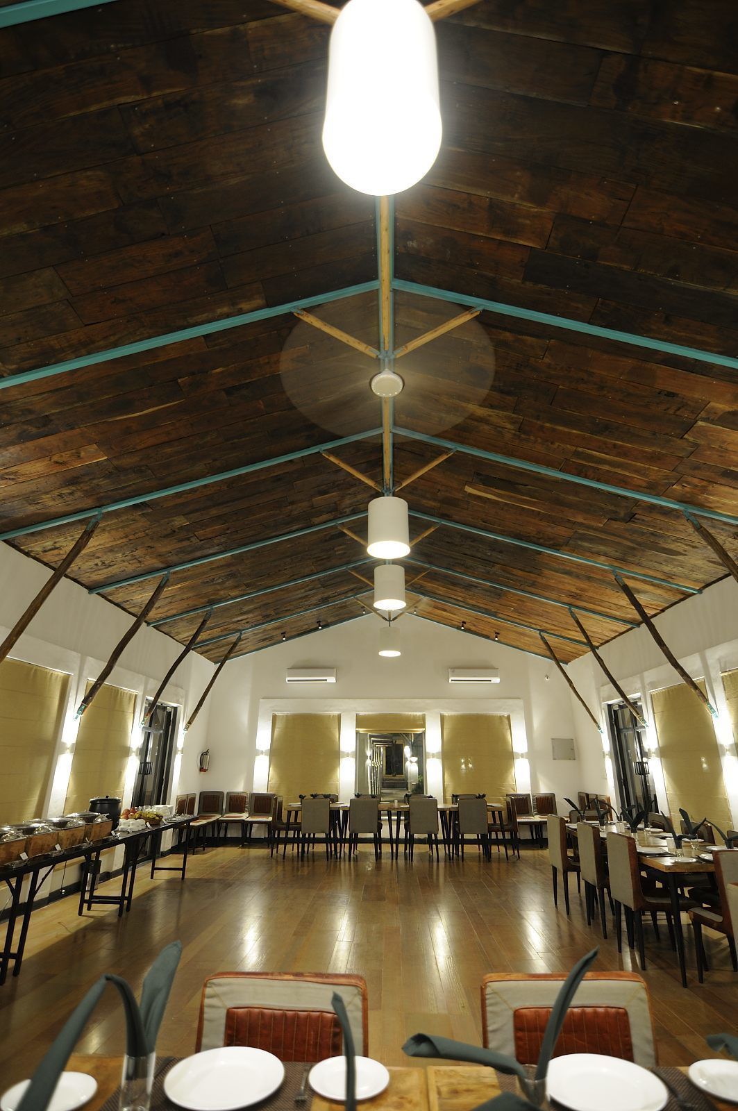 A spacious dining area with high ceilings and exposed beams, featuring multiple tables and chairs arranged for dining.
