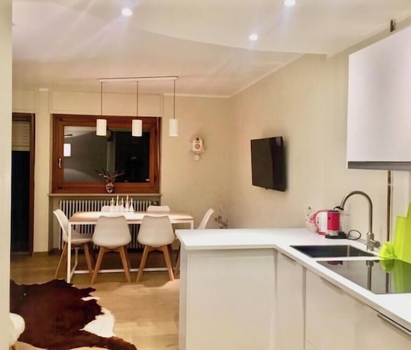 Une cuisine moderne avec un coin repas, un téléviseur fixé au mur et un radiateur placé sous la fenêtre.