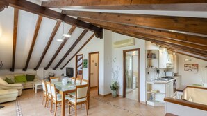Amplia sala de estar con techo alto, vigas de madera, una mesa de comedor con sillas, un sofá y una cocina con armarios y estufa.