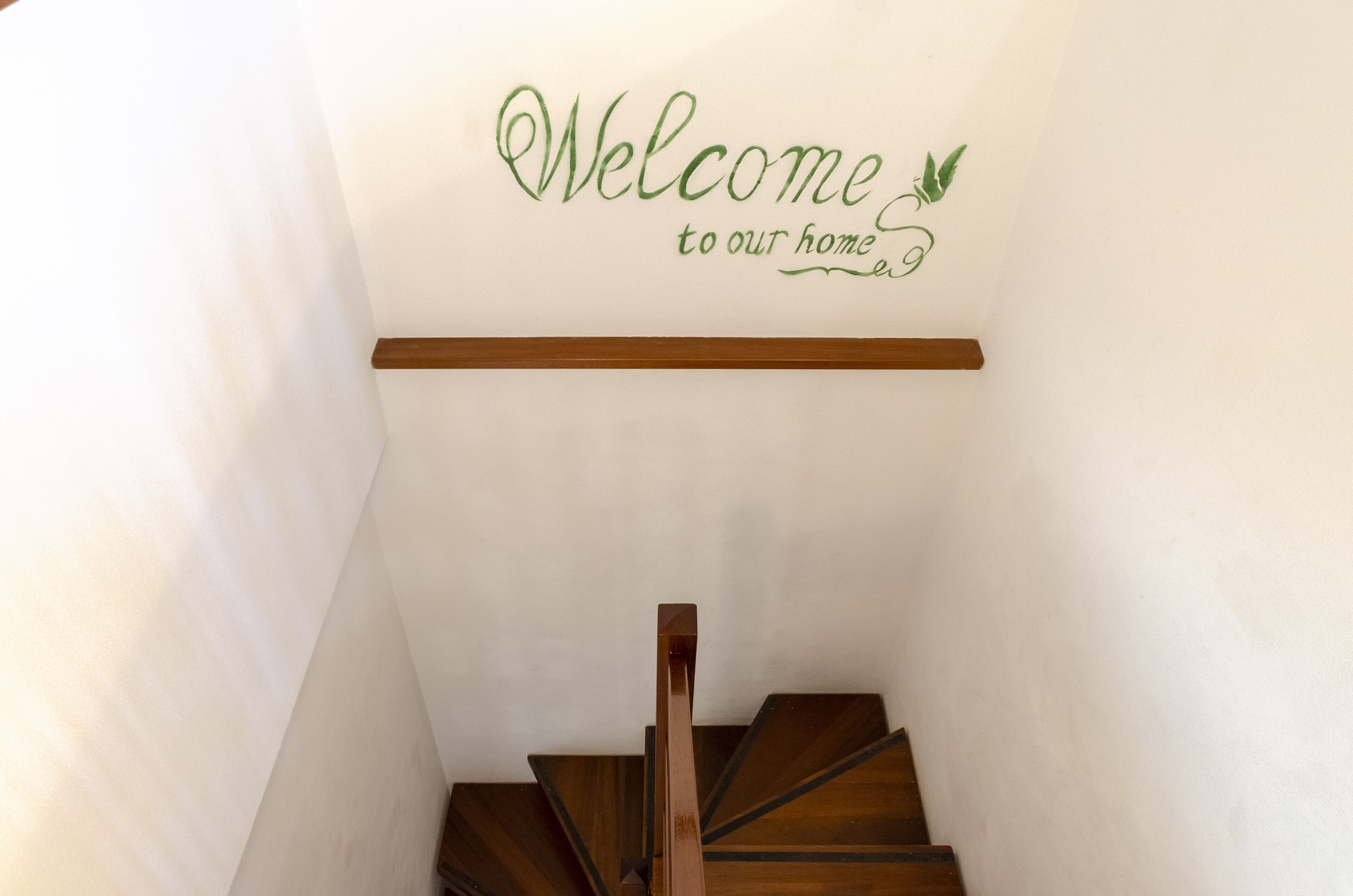 A staircase with a wooden handrail and a wall sign that reads "Welcome to our home."