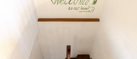 A staircase with a wooden handrail and a wall sign that reads "Welcome to our home."