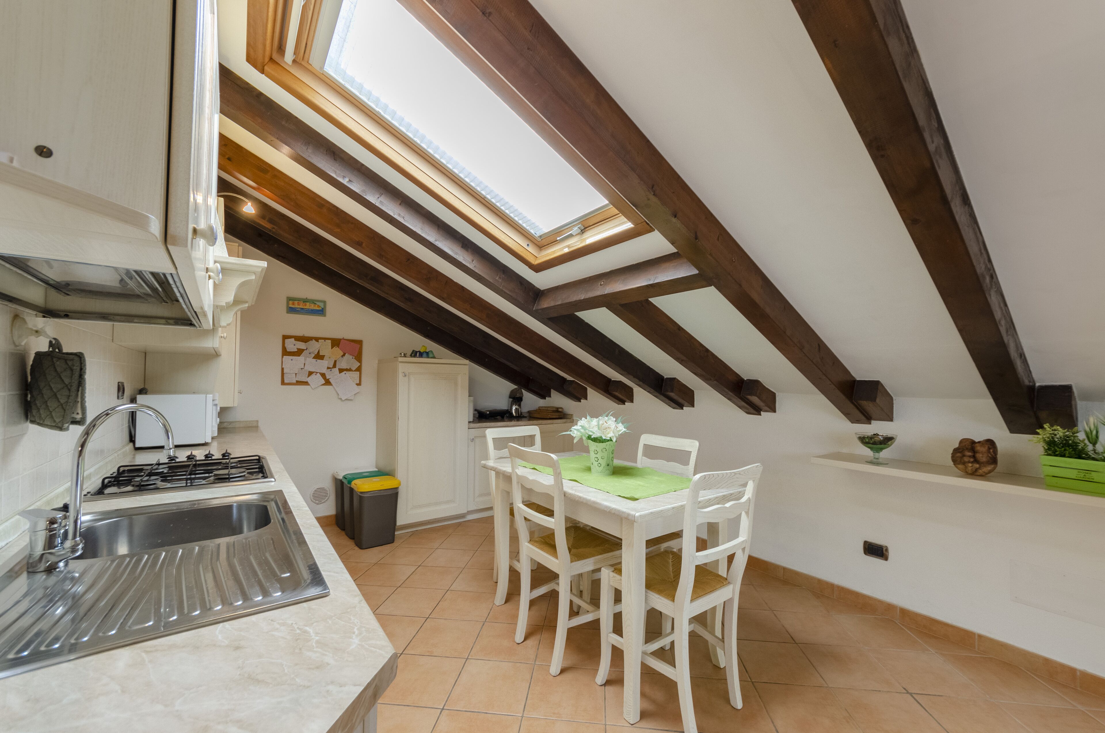 Una cucina con un lucernario, mobili bianchi, un lavello e un'area pranzo con tavolo e sedie.