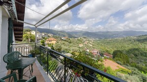 Un balcón con vistas a un paisaje montañoso, una silla verde y una pequeña mesa.