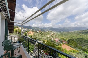 Un balcón con vistas a un paisaje montañoso, una silla verde y una pequeña mesa.