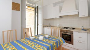 Une cuisine de taille réduite avec des meubles blancs, une cuisinière à gaz et une table à manger recouverte d’une nappe bleue.