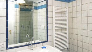 Une salle de bain avec un lavabo blanc, un miroir, une douche et un bidet.