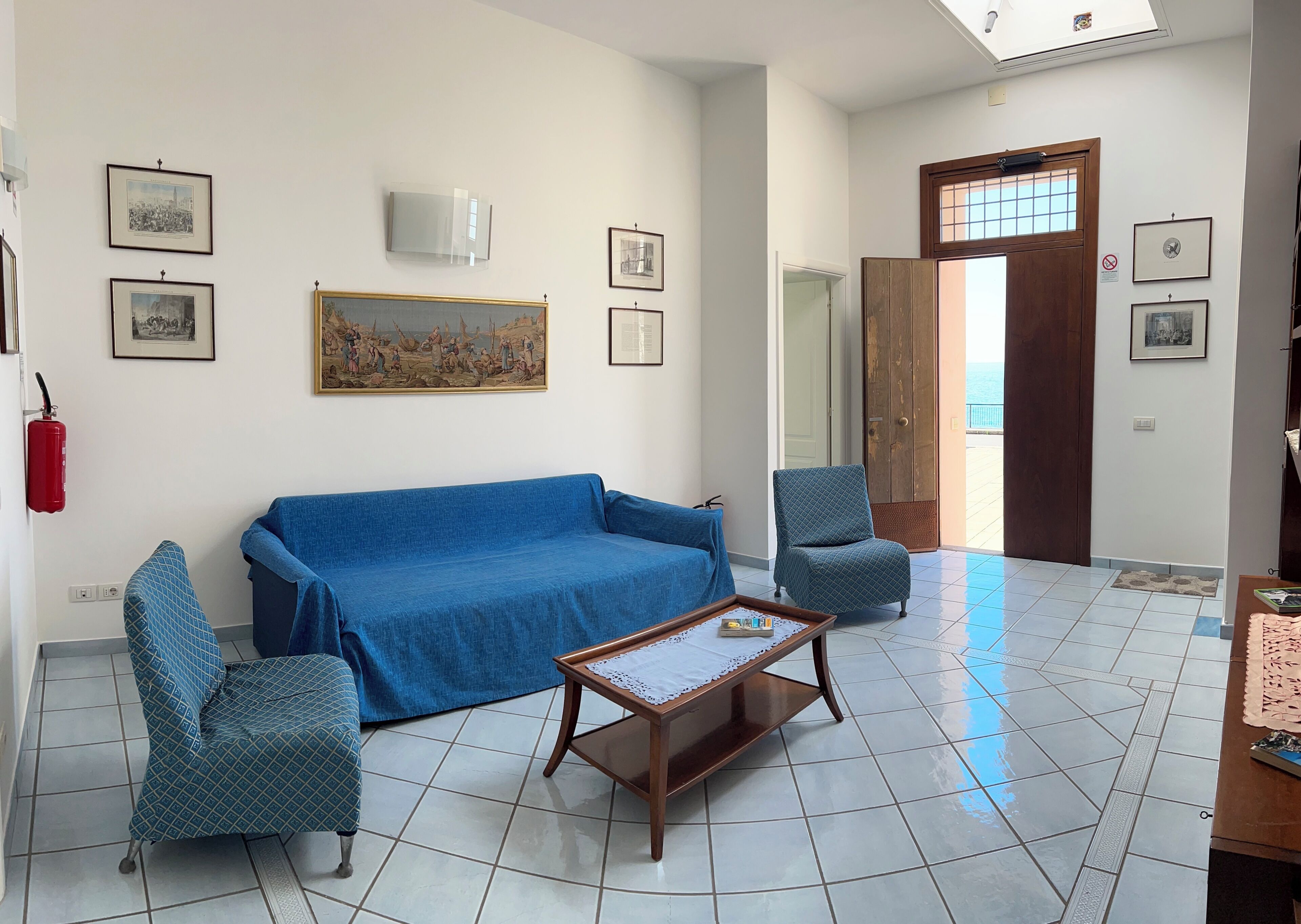 Ein Wohnzimmer mit einer Couch, zwei gemusterten Sesseln, einem Couchtisch und einer zur Außenseite führenden Tür.