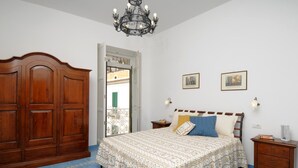 Une chambre avec une grande armoire en bois, un lit avec une literie à motifs, un lustre et deux tableaux encadrés accrochés au mur.