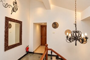 A hallway with a wooden door, a mirror, a wall-mounted clock, a chandelier, and a fire extinguisher. - 10BHK Private Family Friendly Self Catered Villa - 2 min walk to Calangute beach (Calangute)