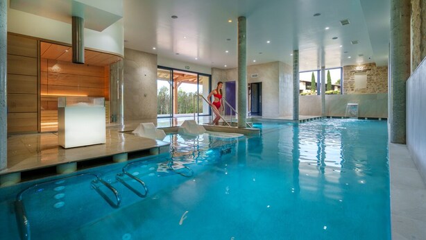 Piscina interna com água cristalina, área de recepção e vista para o exterior.