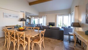 Uma sala de estar ampla com uma mesa de jantar e cadeiras, um sofá e uma televisão.