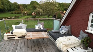 A wooden deck with a built-in sofa and a small table, surrounded by potted plants and a view of a green landscape. - Hos Mette (Borkop)