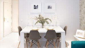A modern dining area with a white table, four chairs, a vase with flowers, and two framed pictures on the wall. - CARRETAS APARTMENTS MADRID 202 (MADRID)