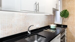 A modern kitchen with white cabinets, a black countertop, a sink, and a backsplash of beige tiles. - CARRETAS APARTMENTS MADRID 202 (MADRID)
