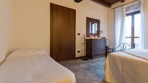 A bedroom with two beds, a wooden door, a dresser, a mirror, and a window with curtains. - Self catering Cà Borgo Vecchio for 3 people (Brusasco)