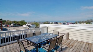 A rooftop deck with a glass table and chairs, overlooking a cityscape and the ocean. - Luxury & Location in New Buffalo - Downtown, Close to Beach, Private Pool (New Buffalo)