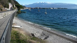 A coastal walkway with a view of a calm sea, boats, and a mountain in the background.