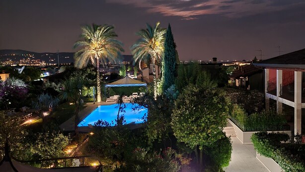 A pool area with a clear view of the surrounding landscape, including palm trees and a building with balconies.