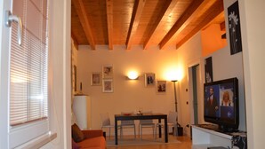 A living room with a wooden ceiling, a dining table with chairs, a television, and framed pictures on the wall.