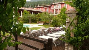 A wooden deck with lounge chairs, a swimming pool, and a red building in the background.