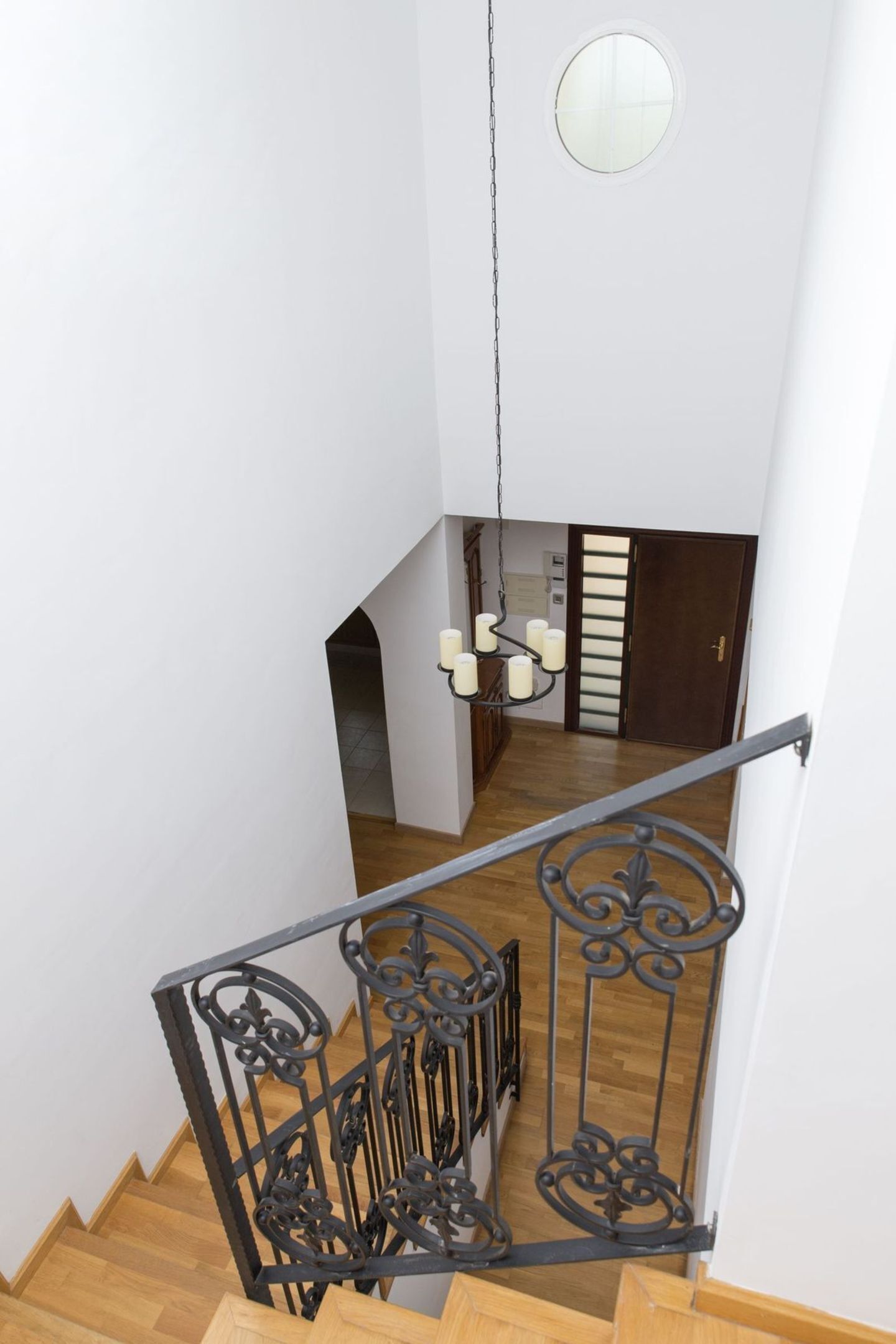 A staircase with ornate black railings, a wooden floor, and a round window at the top.
