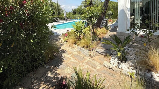 A pool surrounded by lush greenery, a stone pathway, and a white building with a tiled roof. - Villa Pinos de Alhaurin Torre Malaga (Alhaurin de la Torre)