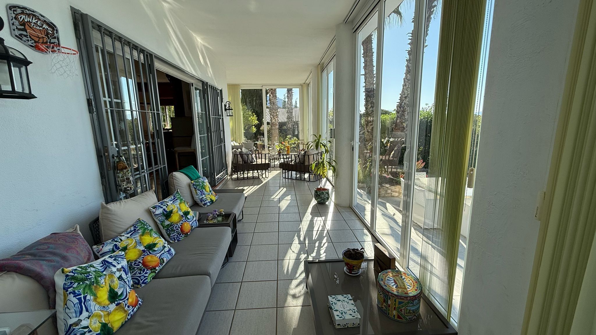 A sunlit balcony with a sofa, potted plants, and a table.