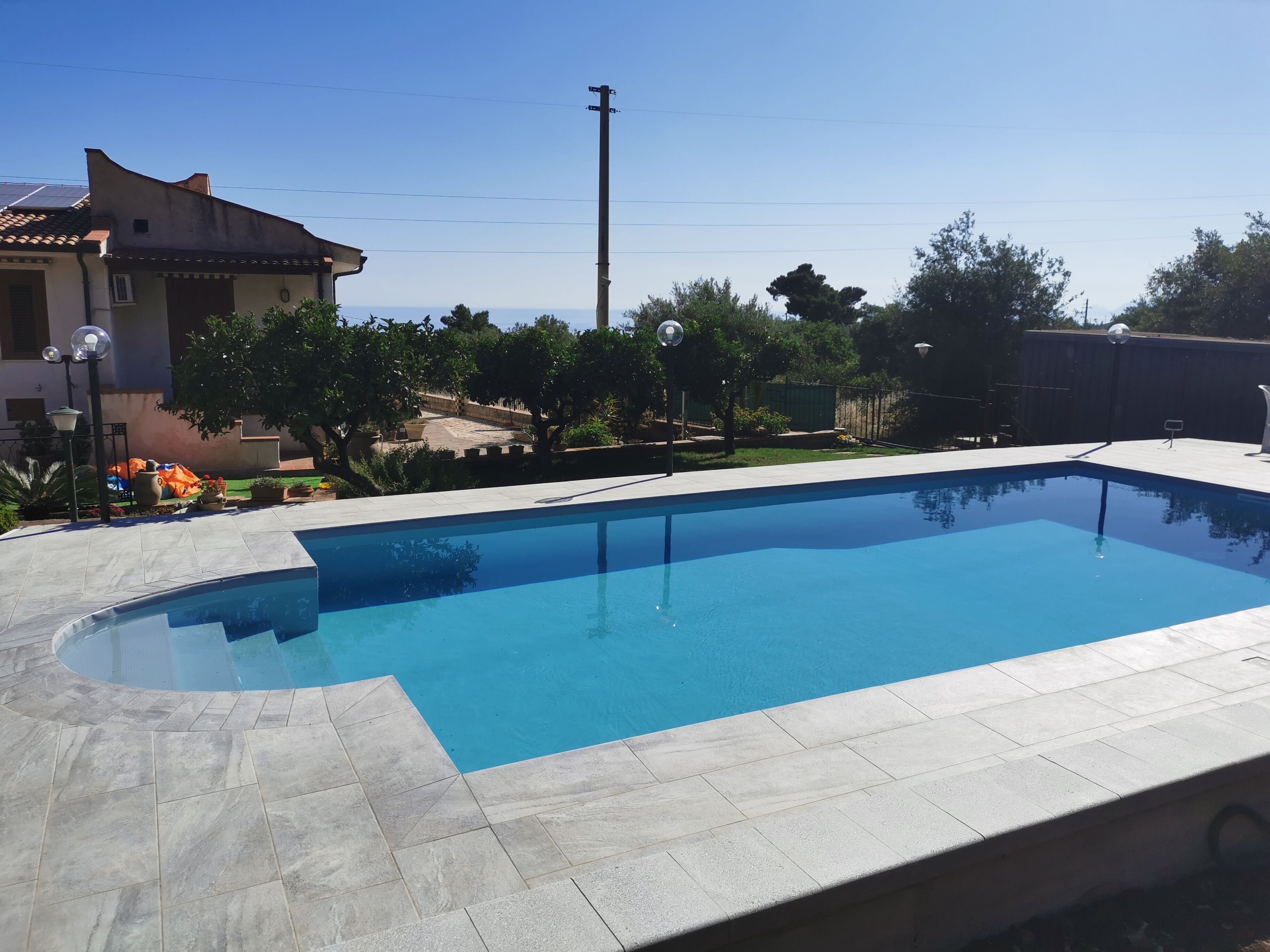 A rectangular swimming pool with a tiled edge, surrounded by a paved deck.